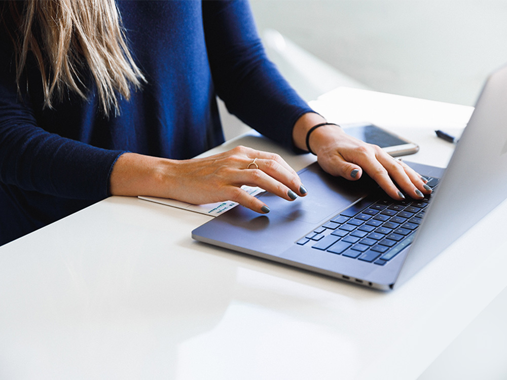 Female typing on a laptop at a white table Female typing on a laptop at a white table