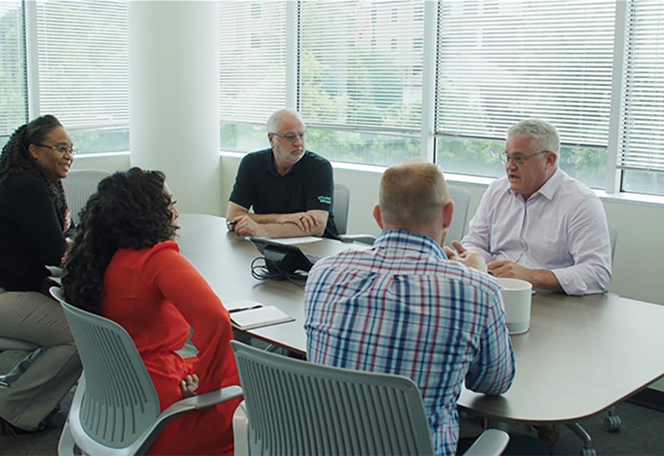 Team of five people sitting around table talking