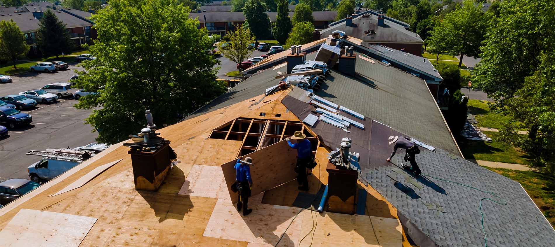 Three workers on apartment building roof installing shingles and tiles